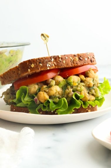 chickpea salad sandwich with sliced tomatoes and a toothpick in the bread.