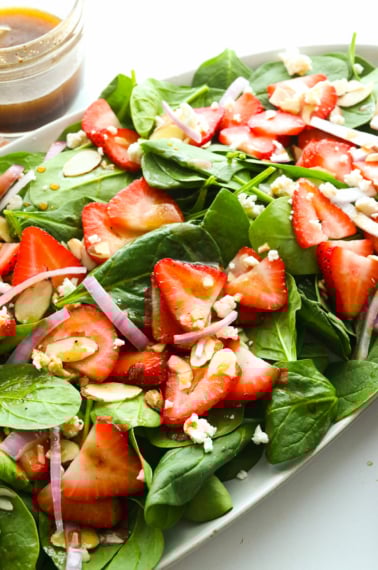 spinach strawberry salad tossed with balsamic dressing on an oval plate.